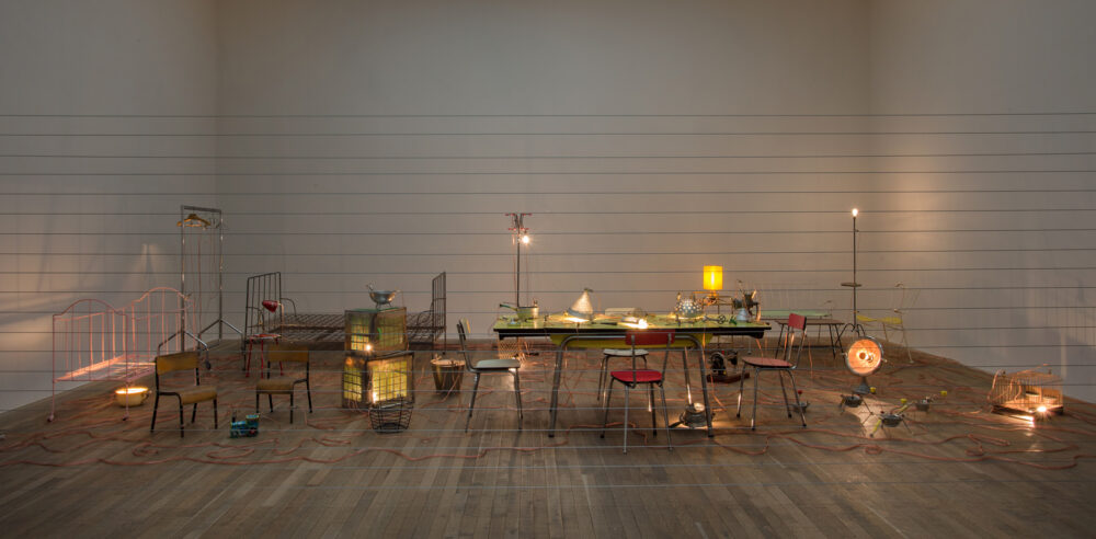 Mona Hatoum, <em>Homebound</em>, 2000. Kitchen utensils, furniture, electric wire, light bulbs, dimmer unit, amplifier, and two speakers. Dimensions variable. Rennie Collection, Vancouver. © Mona Hatoum. Image © Tate Modern, London, 2018. Image courtesy Andrew Dunkley and Seraphina Neville. 